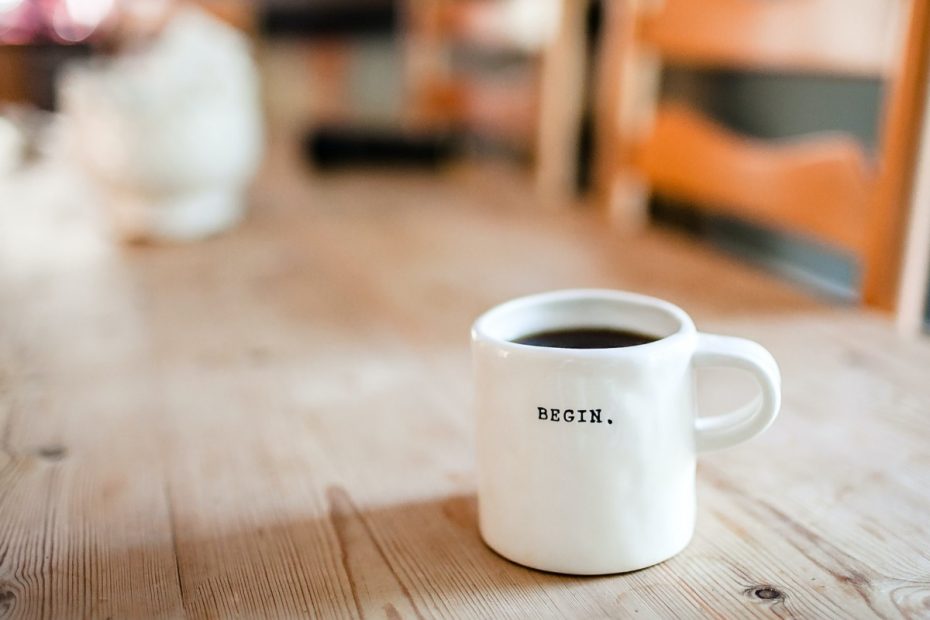 Image of a white mug with the word begin on it on a pine dining room table.