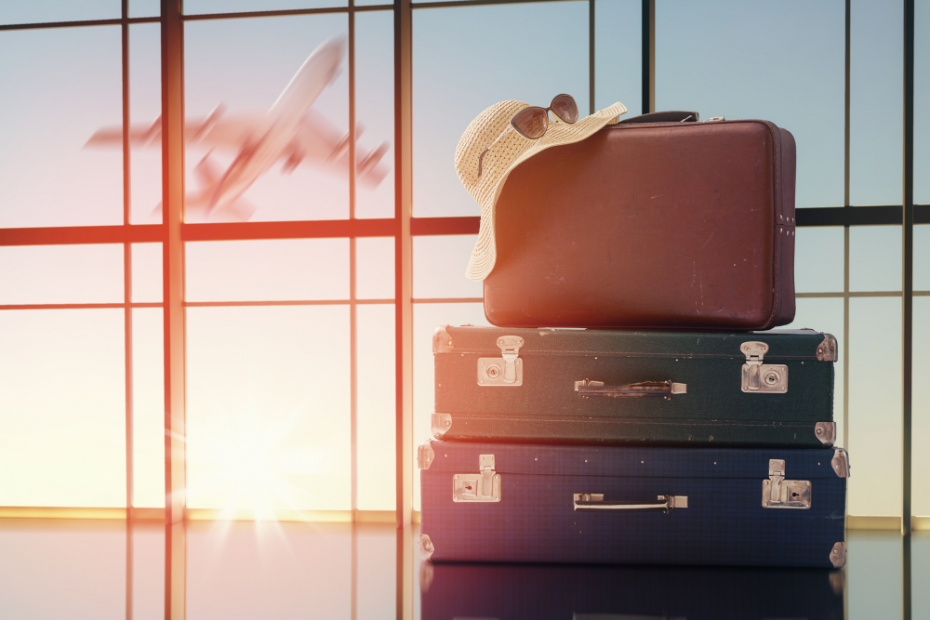 Image of a stack of old style suitcases in front of an airpot window - there's a plane in the background