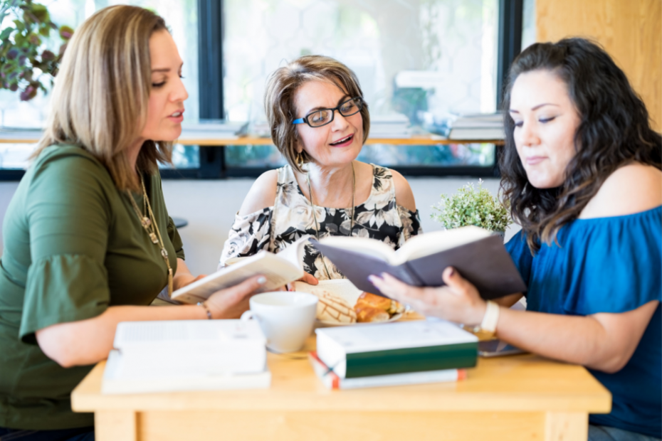 3 women sat together looking at a book in a cafe - accountability buddies