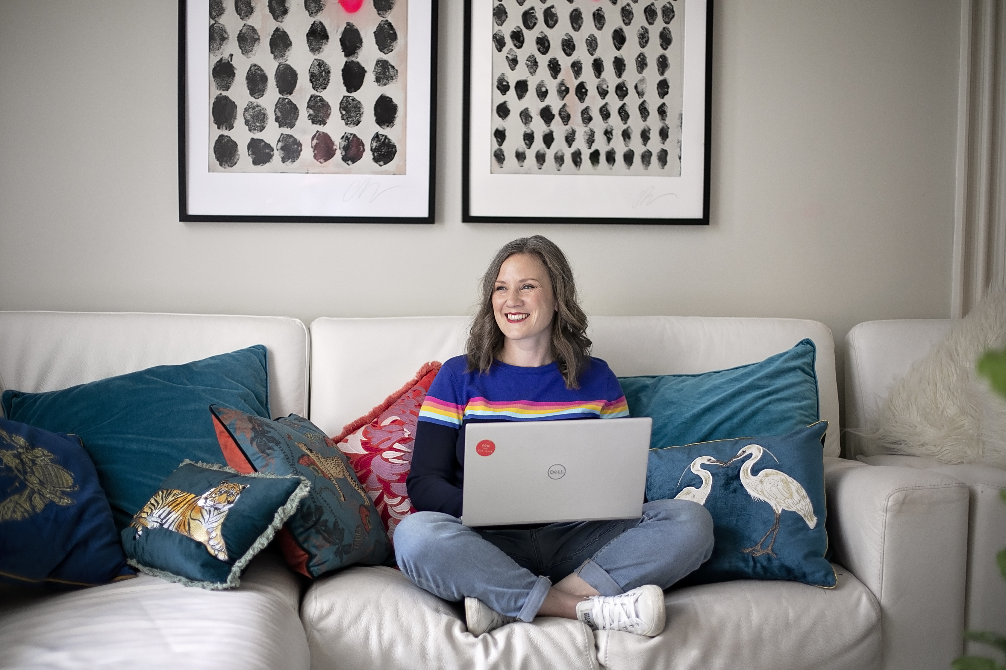 Hannah, a brown haired white woman, is sitting cross legged on a sofa with her laptop on her lap. She's giving the impression of building connections with her mailing list