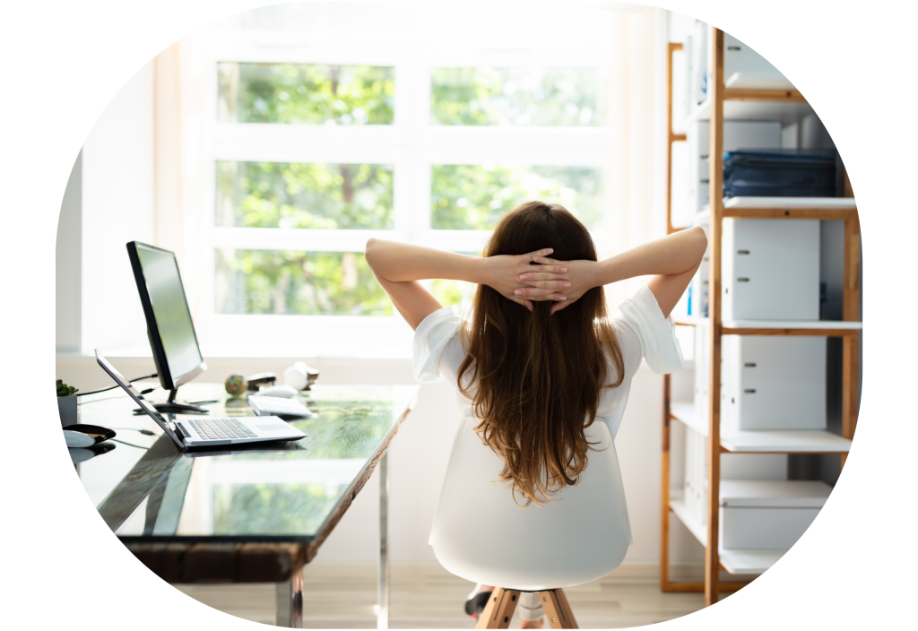 Image of a woman, taken from behind, she is sitting by her desk, looking out the window with her hands behind her head. The image gives the impression she is very relaxed as she has outsourced to a virtual assistant!