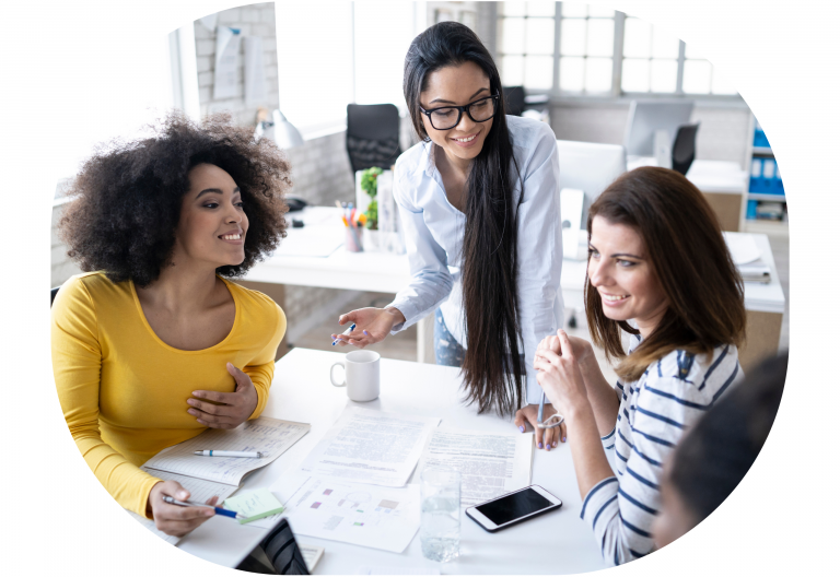 Image of 3 women at a desk with laptops open, talking & smiling looking like they are discussing business, outsourcing & freelance life