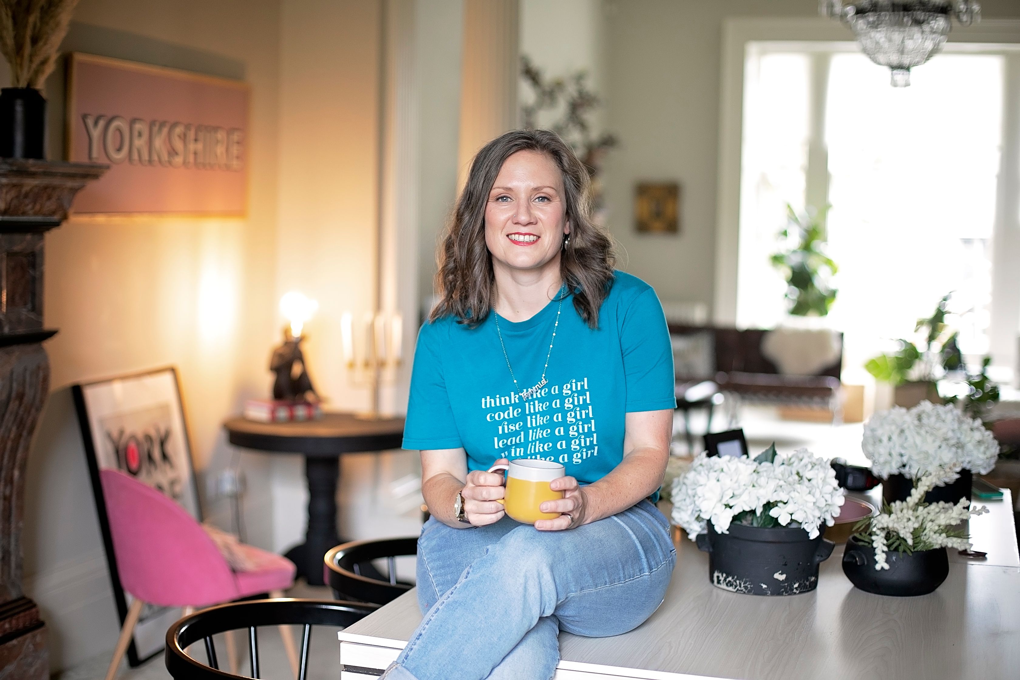 Hannah sitting on a table with a cup of tea looking at the camera