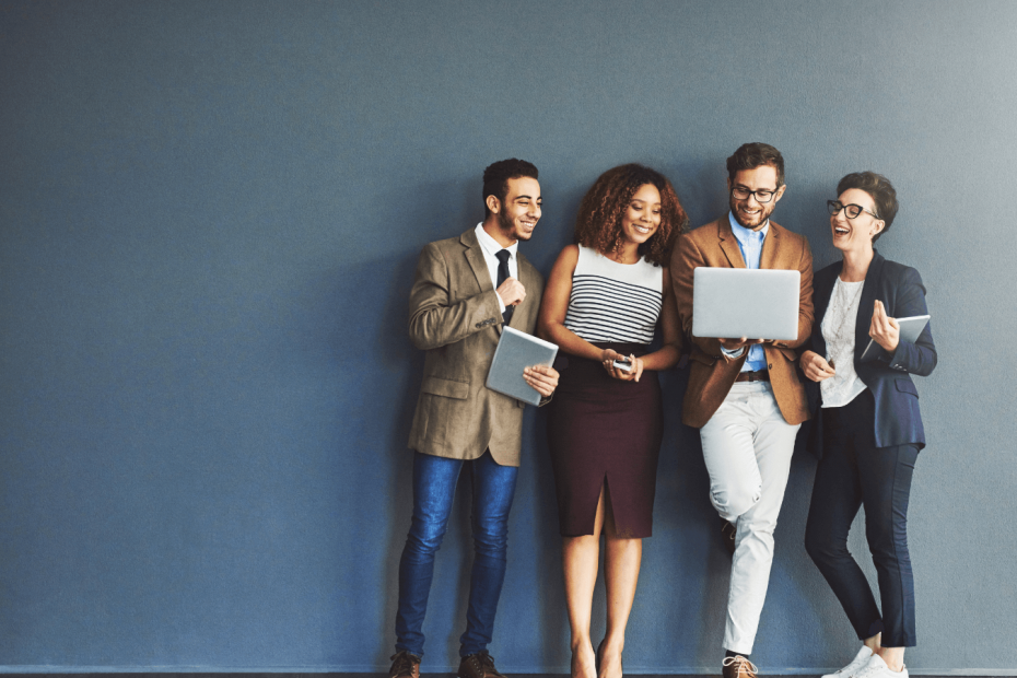 Studio shot of a group of business people standing together smiling & chatting while looking at a laptop as they are reading an email that has arrived via a mailing list