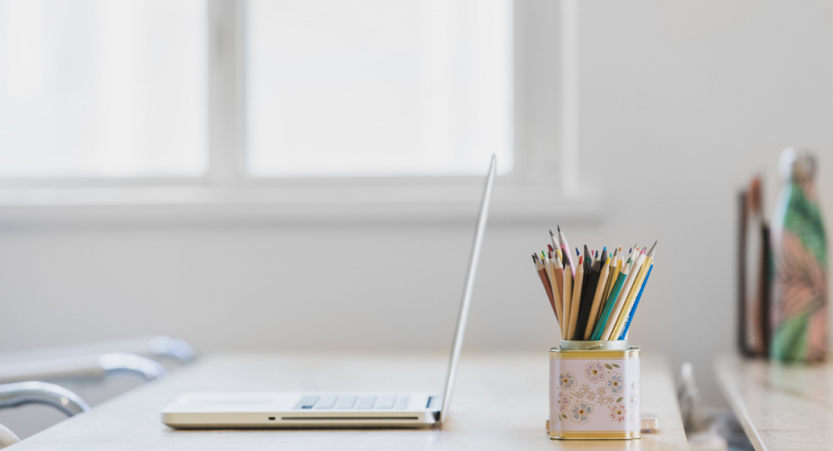Clean image of a desk, laptop & pencil pot. There is a lot of white space, to give the impression of a productive workspace